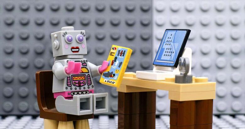 Lego robot minifigura con instructivo sentada frente el computador
